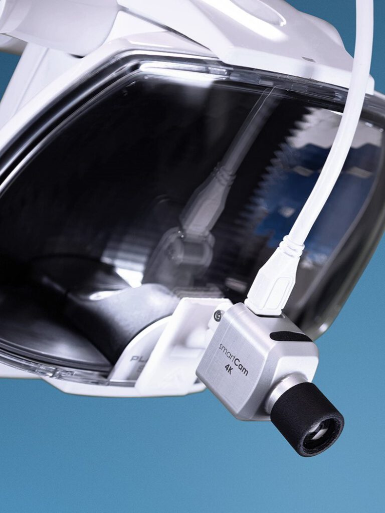 Silberne 4K-Kamera mit der Aufschrift 'smartCam 4K', montiert an einer medizinischen Lampe. Die Kamera ist mit einem weißen Kabel verbunden.